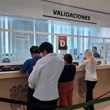 Movilidad y Transportes - Una larga fila de personas espera para ser atendidas en una oficina de Validaciones, dividida en módulos designados por letras