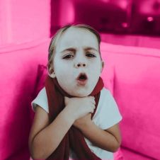 Niña tosiendo sobre un fondo rosa